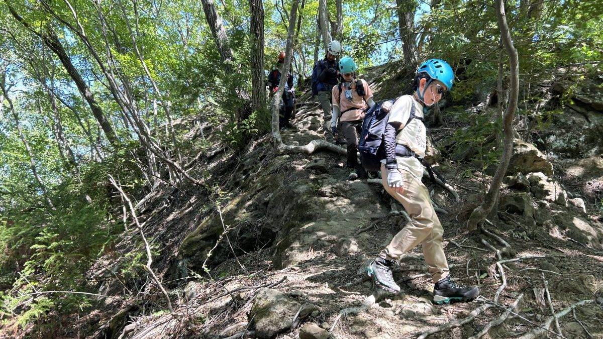 Hikers wearing helmets carefully descending a rocky forest trail.