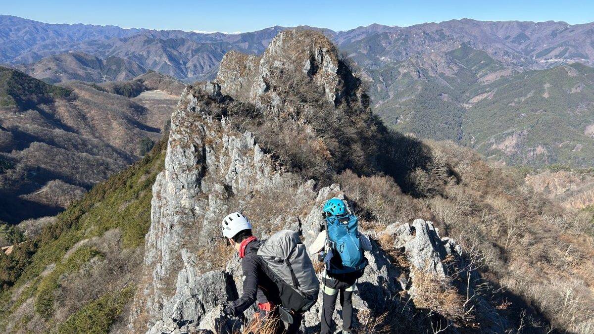 Group of climbers wearing helmets and backpacks crossing a rocky mountain ridge with expansive valley below.