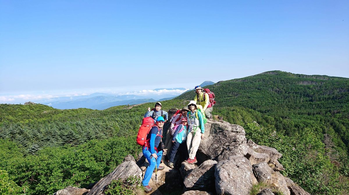 山並みを見渡す岩場で、親子で登山を楽しむ参加者たち