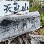 Weathered wooden trail sign with Chinese characters mounted on a rough log amid rocky, forested terrain.