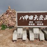Sign at the summit of Mount Hakkoda with elevation 1,585 m, supported by concrete blocks and a stone cairn nearby.