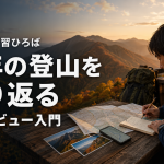 山岳を背景に地図に記録をつける登山者。木のテーブルに写真とスマホ、背後は夕暮れの山々。背中にリュック。