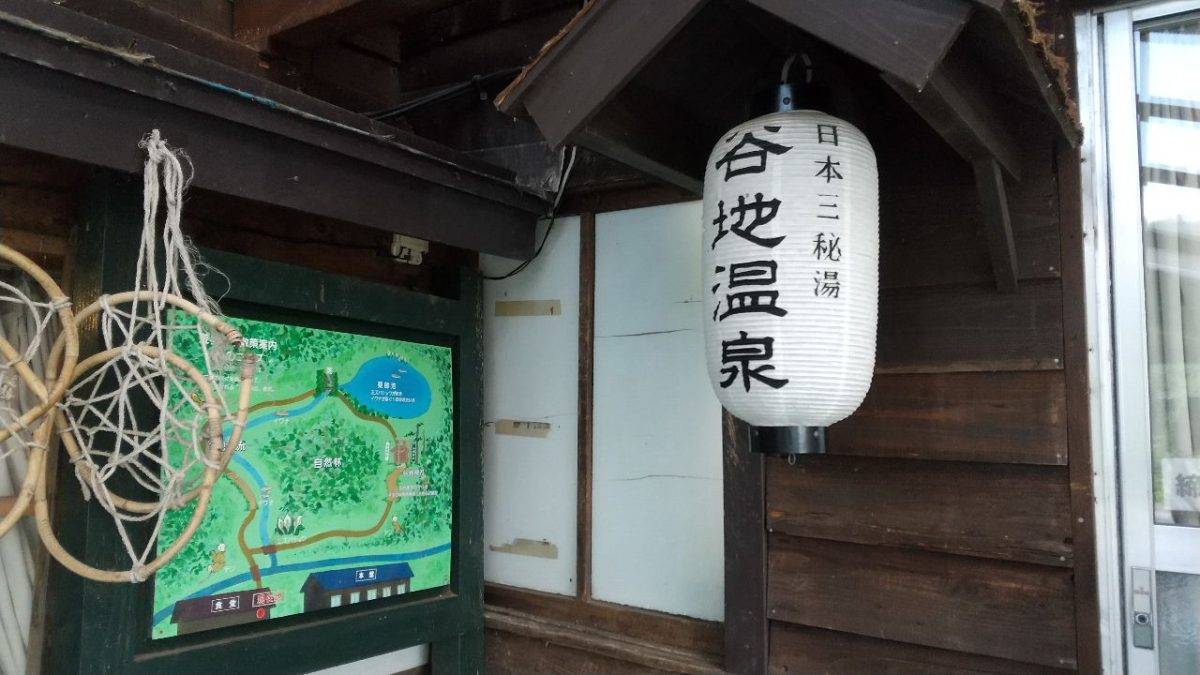 White paper lantern with Japanese characters hanging outside a wooden building beside a colorful map sign (hot spring area).