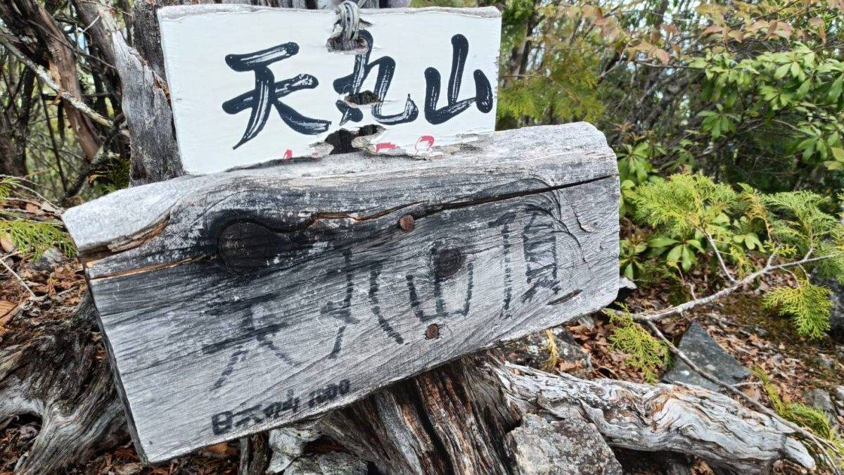 Weathered wooden trail sign with Chinese characters mounted on a rough log amid rocky, forested terrain.